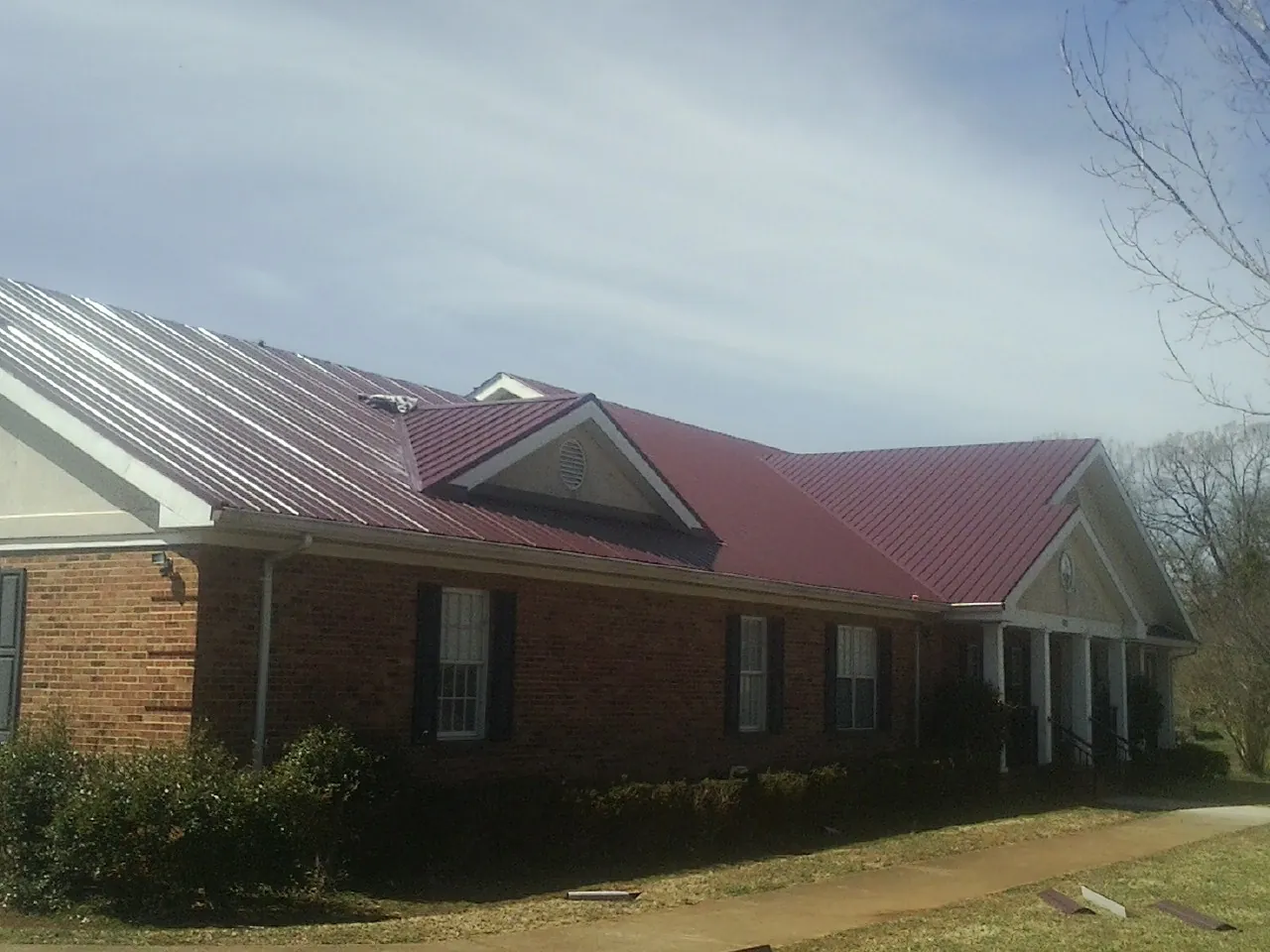 Red metal roof with gabled entries on a long brick building, from a Hail Damage Roof Repair job in Hockingport