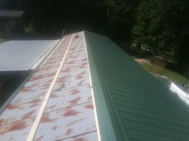 Old rusted panels beside newly installed green metal roofing — Wind Damage Roof Repair by Roofing Brothers in Hockingport