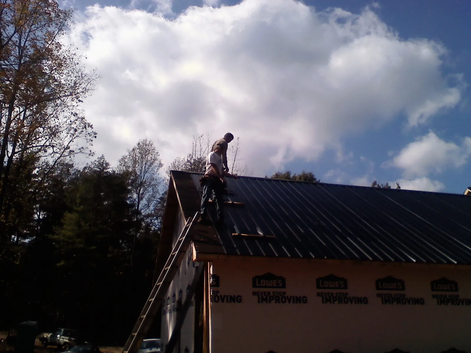 Roofer fastening dark metal panels high against a cloudy sky, from a Roof Inspection job in Hockingport