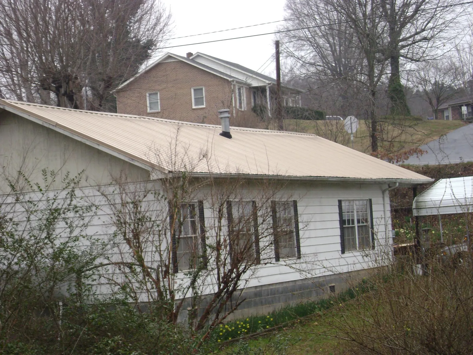 Tan metal roof on a white sided house set into a hillside — Commercial Roofing by Roofing Brothers in Hockingport